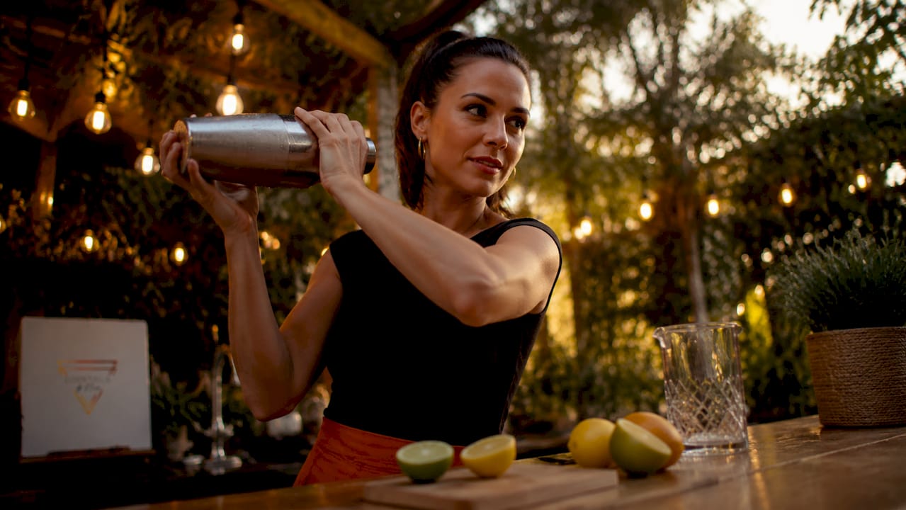 Een bartender staat energiek te shaken achter de bar, terwijl hij een cocktail bereidt.