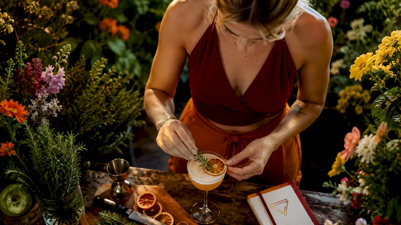 Een bartender werkt zijn cocktail af met een takje munt en een sliertje citrusschil.