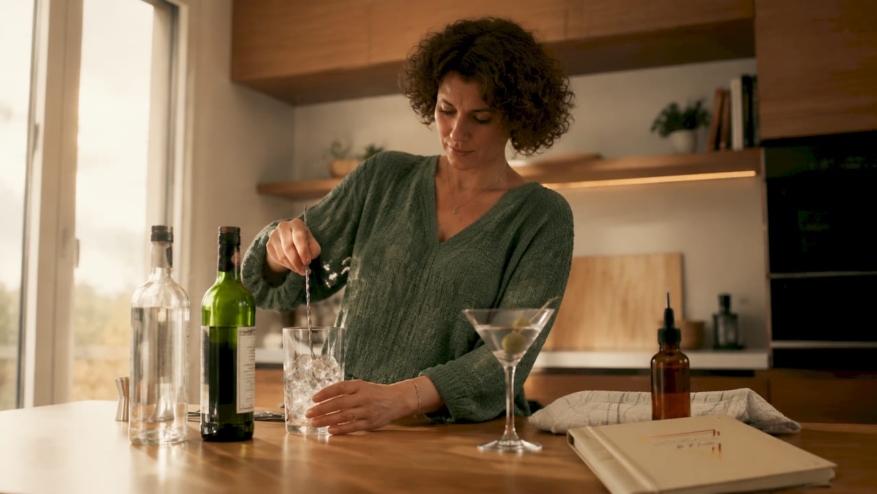 Een vrouw die thuis achter haar eigen bar een martini voorbereidt en roert.