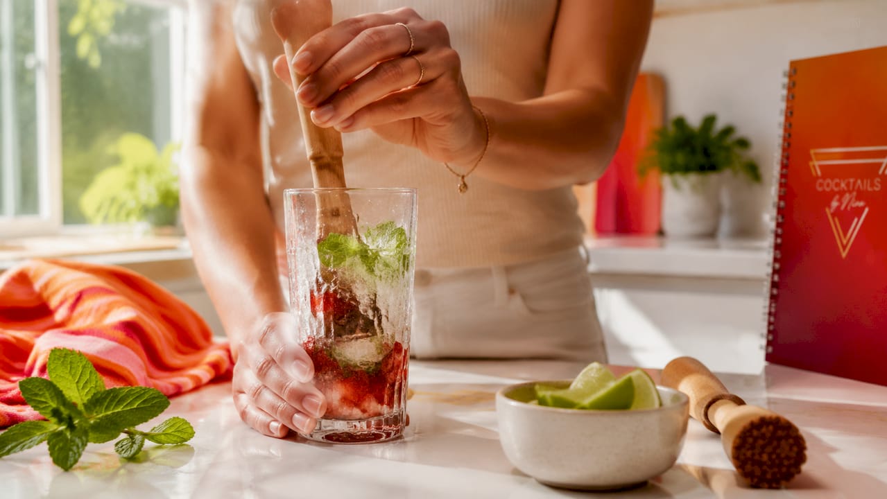 Met de handen worden verse munt en aardbeien in een glas gekneusd.