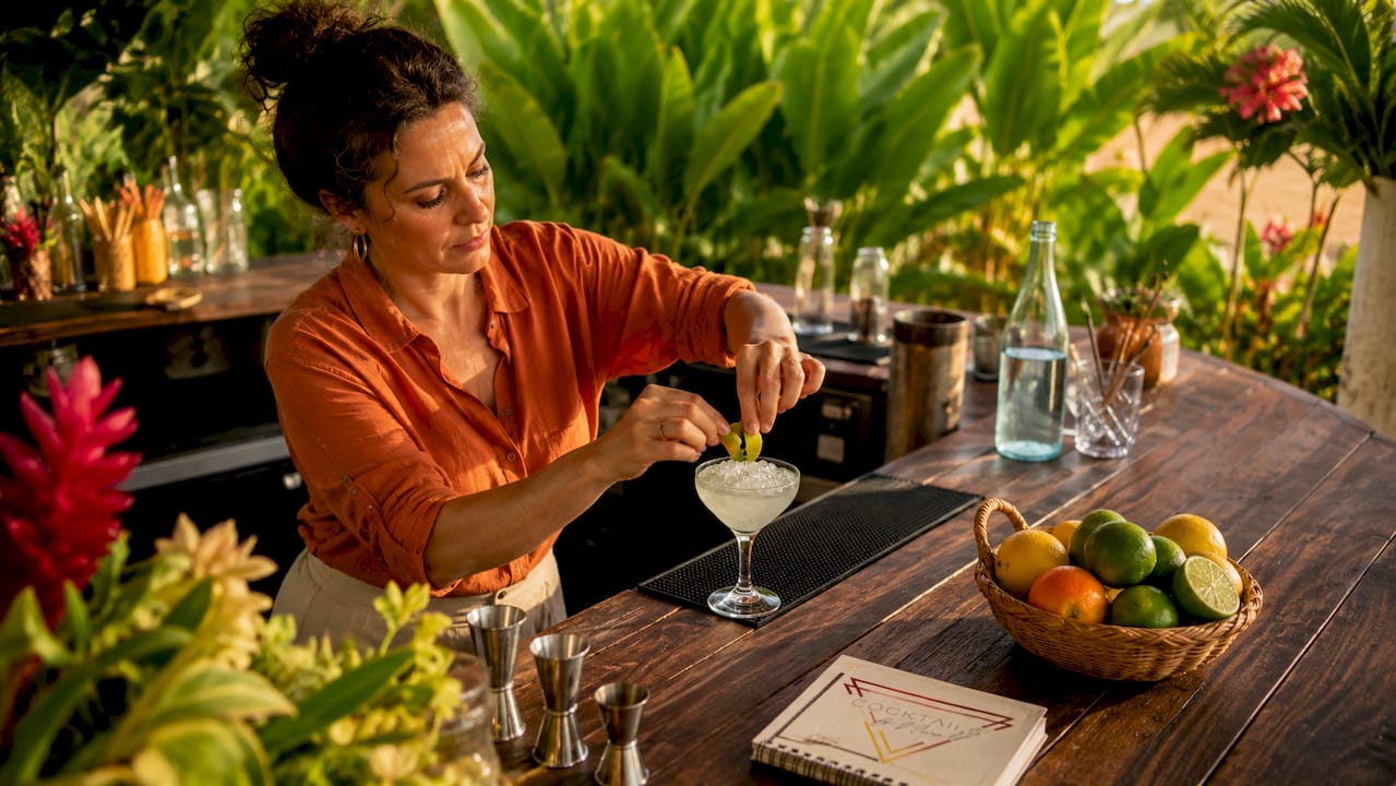 De barman werkt met aandacht en voegt als finishing touch een stukje citroenschil toe aan de cocktail.