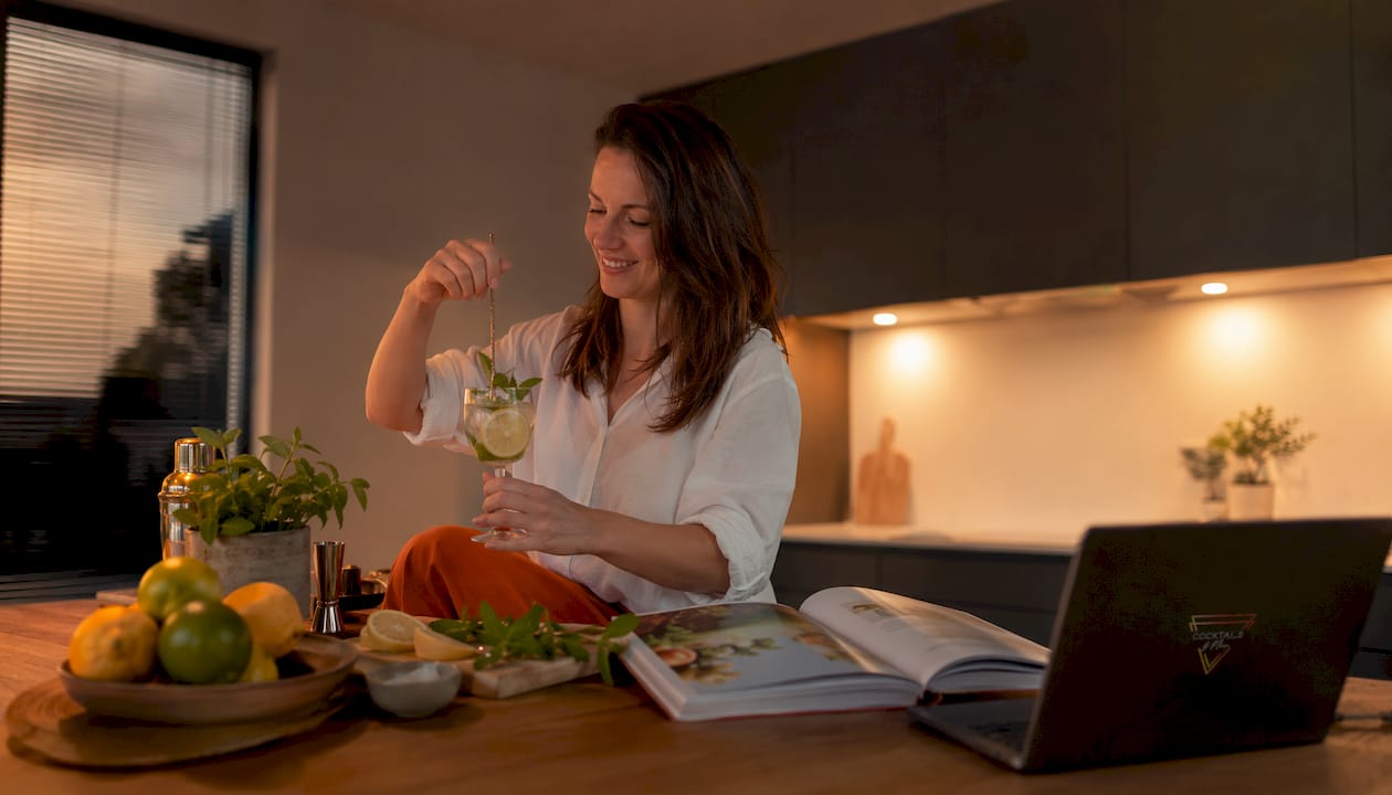 Een vrouw geniet thuis van een ontspannen moment met een cocktail in haar hand.