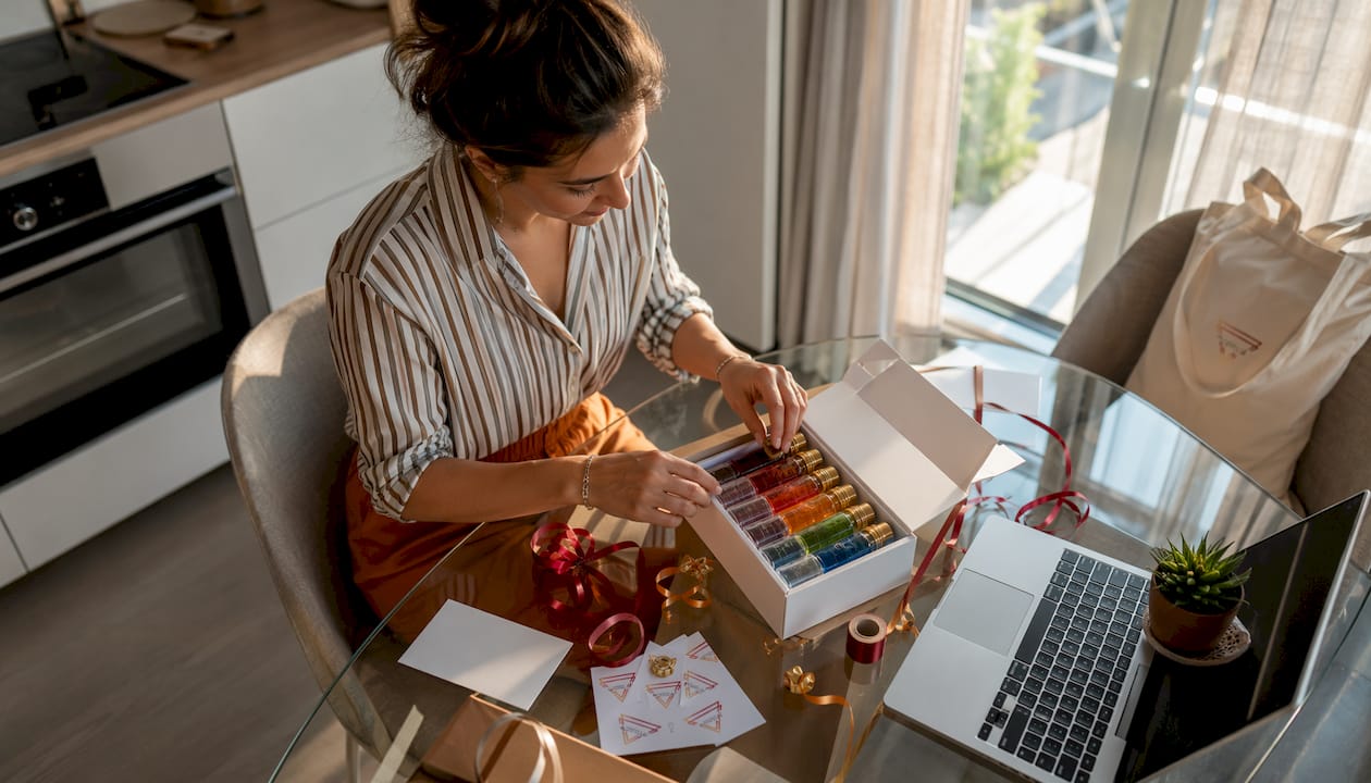 Een vrouw is thuis aan de keukentafel bezig met het samenstellen van een cadeaupakket met shotjes.