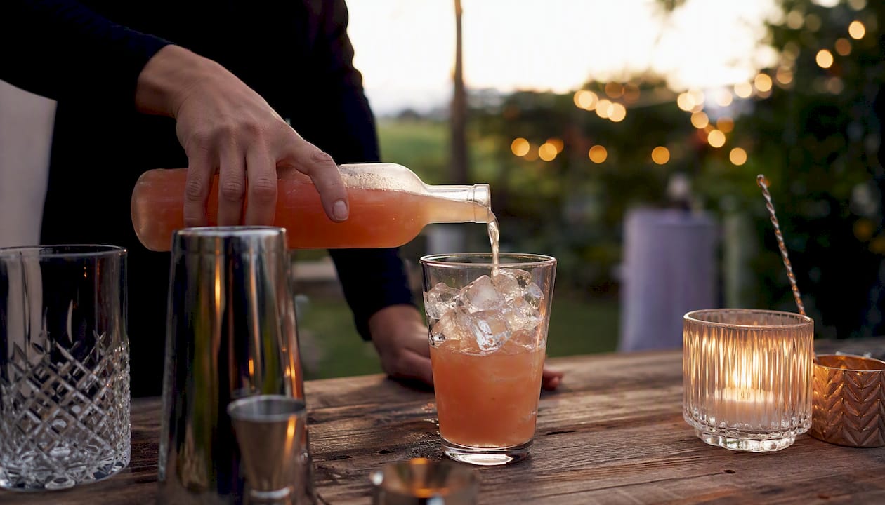 Een hand schenkt een kant-en-klare cocktail uit in een glas.