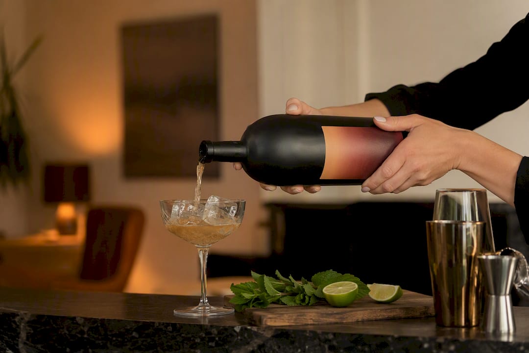 Een hand schenkt een kant-en-klare cocktail uit achter de bar.