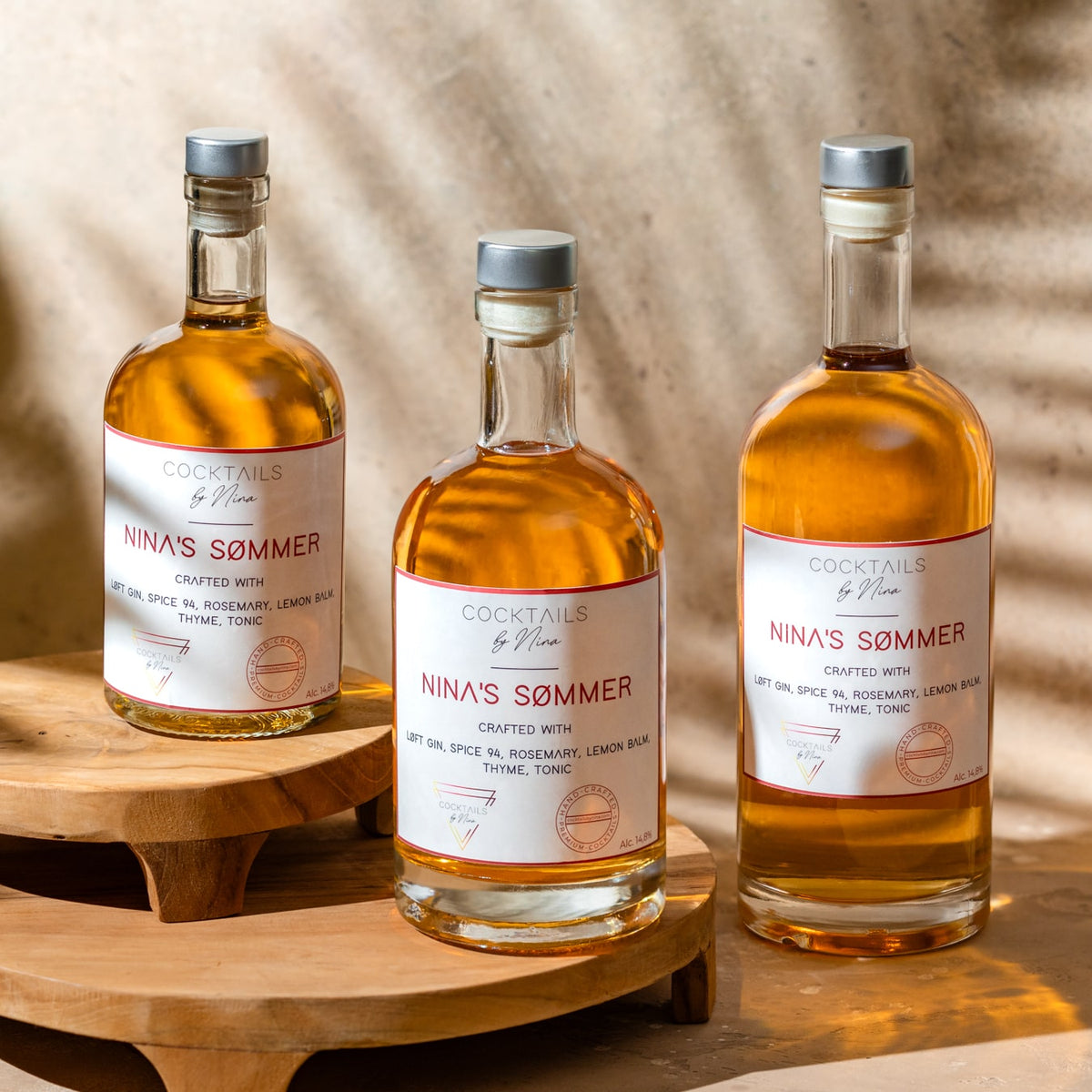 Three bottles of Nina's Sømmers cocktails, featuring amber liquid and labels detailing ingredients on a wooden display.-Cocktails by Nina