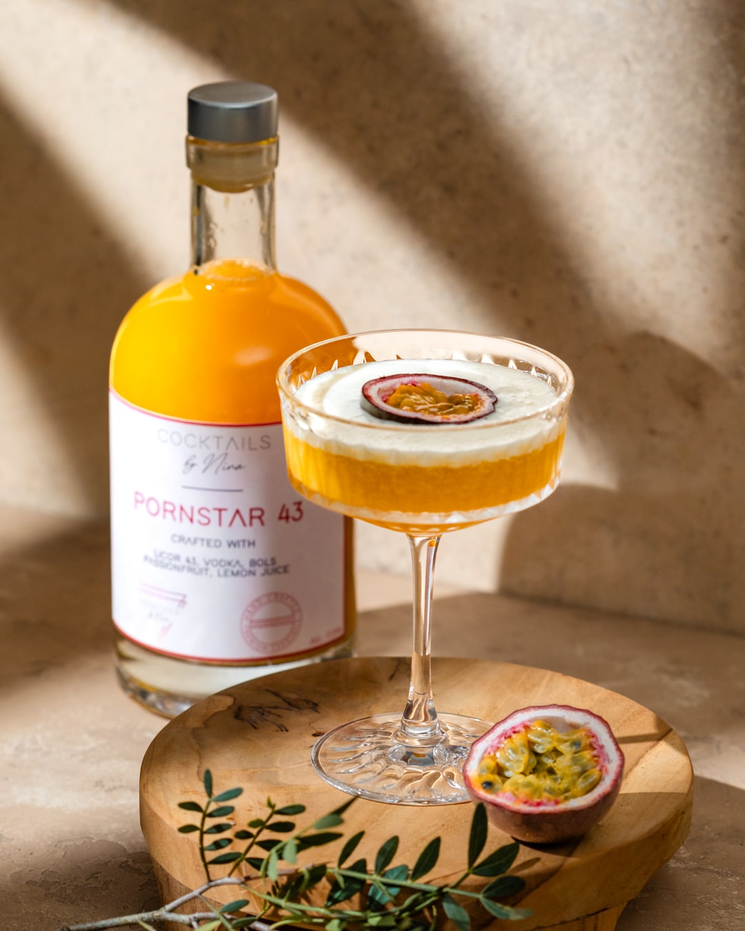 Cocktail named Pornstar 43 in a glass with passion fruit garnish, alongside a bottle on a wooden board.-Cocktails by Nina
