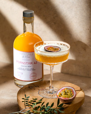 Cocktail named Pornstar 43 in a glass with passion fruit garnish, alongside a bottle on a wooden board.-Cocktails by Nina